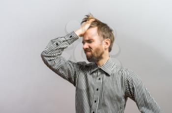 Young handsome man holding his head frustrated. Gesture. On a gray background