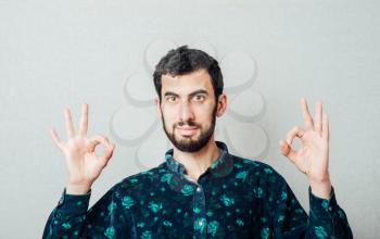 Everything is OK! Happy young man in shirt  gesturing OK sign and smiling while standing against grey background