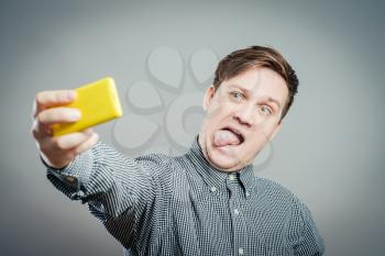 Handsome young man in shirt holding camera and making selfie and smiling while standing against grey background