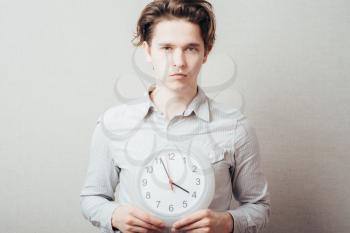 Portrait Of A Young Man Holding A Clock On Gray Background