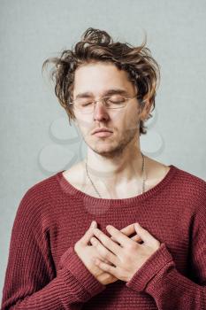 The man in glasses hands together praying. On a gray background.