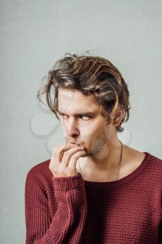 Man thinks upset with his hand to his mouth. On a gray background.