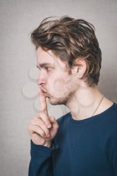 A man shows a finger to his mouth quiet. On a gray background.