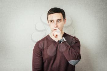 Portrait of the young thinking man looks up with hand near face