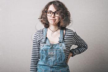 Woman in overalls dissatisfied stands with hand on hips. Gray background.