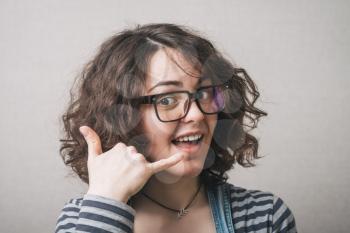 Woman in glasses makes a gesture call me. Gray background