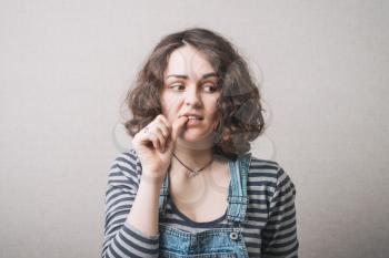 The woman lost in thought, chewing on nails from experiences fear. On a gray background.