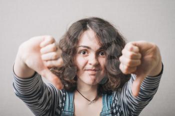 Woman showing two thumbs down. On a gray background.