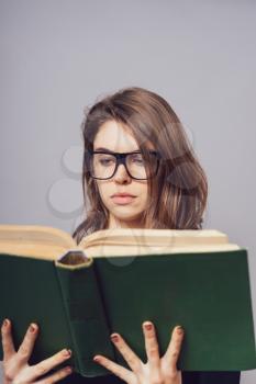 girl with glasses reading a book, looking from her