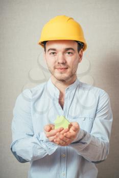 Young guy in a helmet holding a house made of paper. 