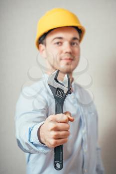 The man in yellow helmet with a wrench. On a gray background.