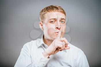 Business man with finger on lips asking for silence over gray background