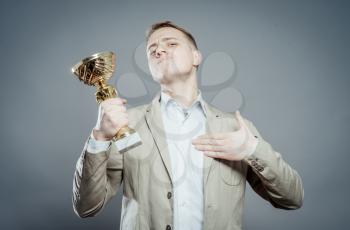 a winner with suit holding a cup/trophy shows itself with pride over gray