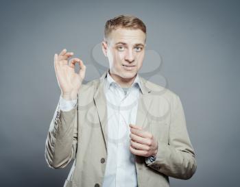 Young man gesturing OK sign on gray background