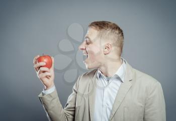 Cheerful beautiful man eating apple, isolated over gray background