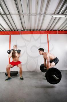 Group of two people exercising using barbells in gym and kettlebell crossfit workout 
