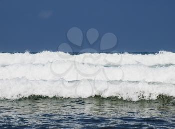 Three ocean waves breaking with clean blue sky in the background