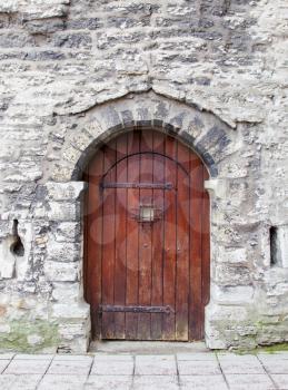 Old wooden arched door in stone wall.