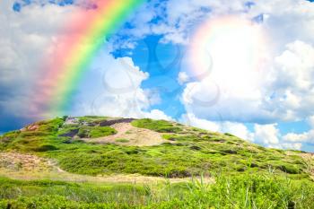 Summertime green hill background with bright sun and rainbow.