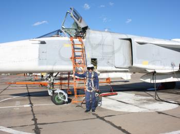 The military pilot in the plane in a helmet in dark blue overalls against the blue sky