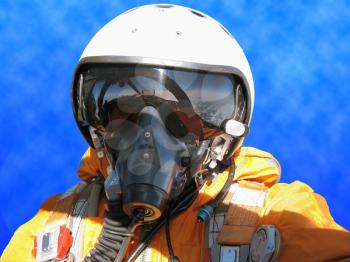 The military pilot in the plane in a helmet in dark blue overalls against the blue sky