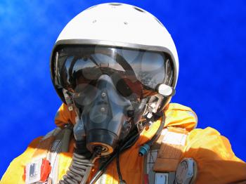 The military pilot in the plane in a helmet in dark blue overalls against the blue sky