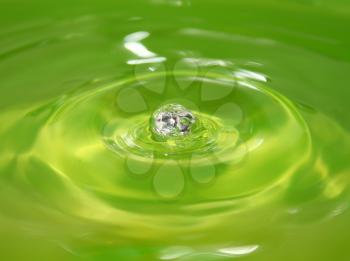The green drop of water falls leaving circles on a surface being reflected and sparkling