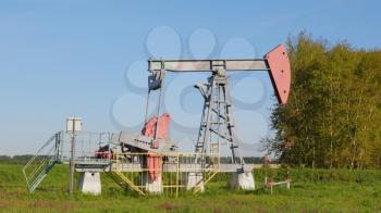 Operating oil and gas well in oil field, profiled against the blue sky.