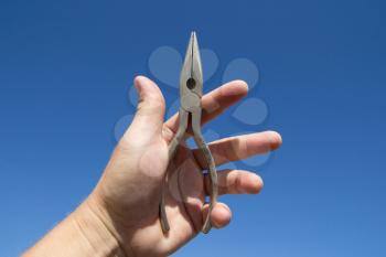 Pliers in hand man on a background of blue sky