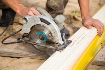 worker saws a wooden plank at a construction site .