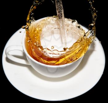 tea being poured into a saucer with splashes on a black background