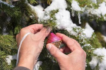 man hangs a toy on the Christmas tree in winter