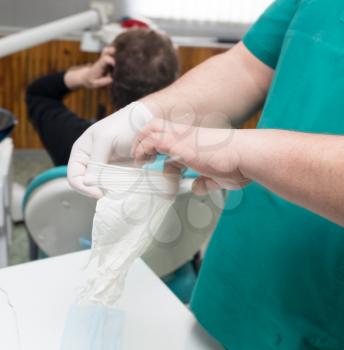 Doctor dentist puts on white gloves in the clinic .