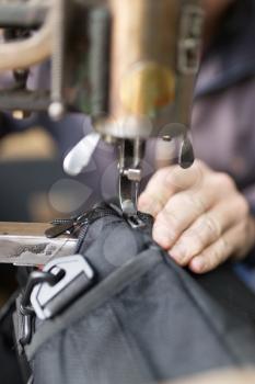 Tailor man sews up a bag in a workshop .