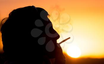 Silhouette of male smokers in the sunset .