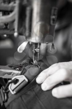 Tailor man sews up a bag in a workshop .