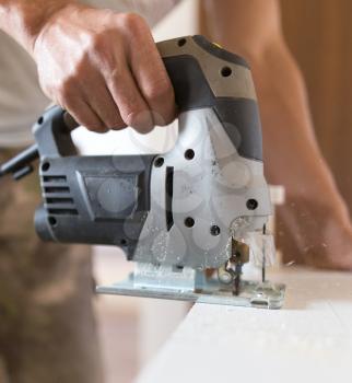 A man cuts out a wooden board with a jigsaw .