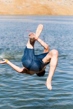 A man dives from shore to lake .