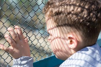 The boy stands near the metal fence .