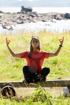 Beautiful girl in a red dress sitting on a bench in the lotus position