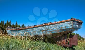old wooden fishing boat on the beach in the coastal grass with blue sky and forest