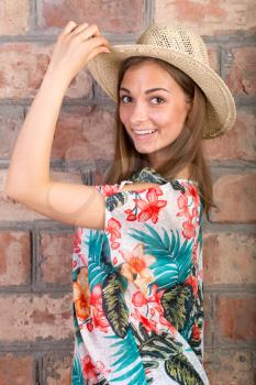 The beautiful girl in a summer hat against a brick wall. Studio portrait