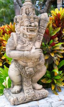 Thai stone god in the bushes of tropical plants. Short depth of field.