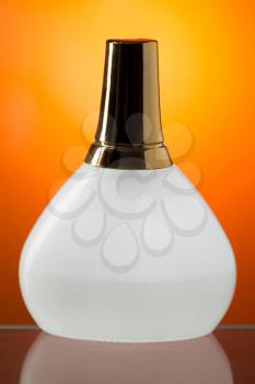 White bottle stands on the mirror surface. Orange background