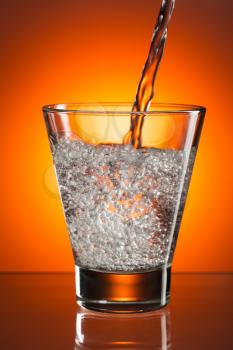 In the glass of mineral water are poured. Against a bright orange light spot with a smooth gradient.