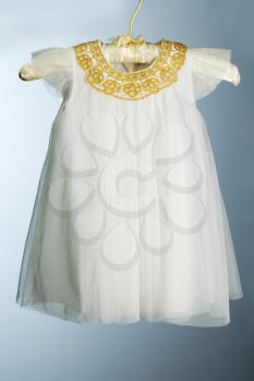 Elegant white baby dress decorated with gold. On a gray gradient background.