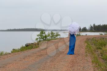 Slim girl in a dress with an umbrella in a forest on a country road