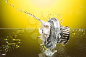 Auto parts, engine cooling pump in water splash on yellow gradient background