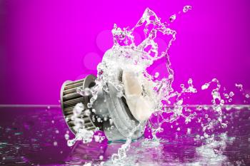 Auto parts, engine cooling pump in spurts of water on purple gradient background