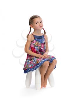 Little girl in a colored dress on a chair in the studio and shy, isolate on white.